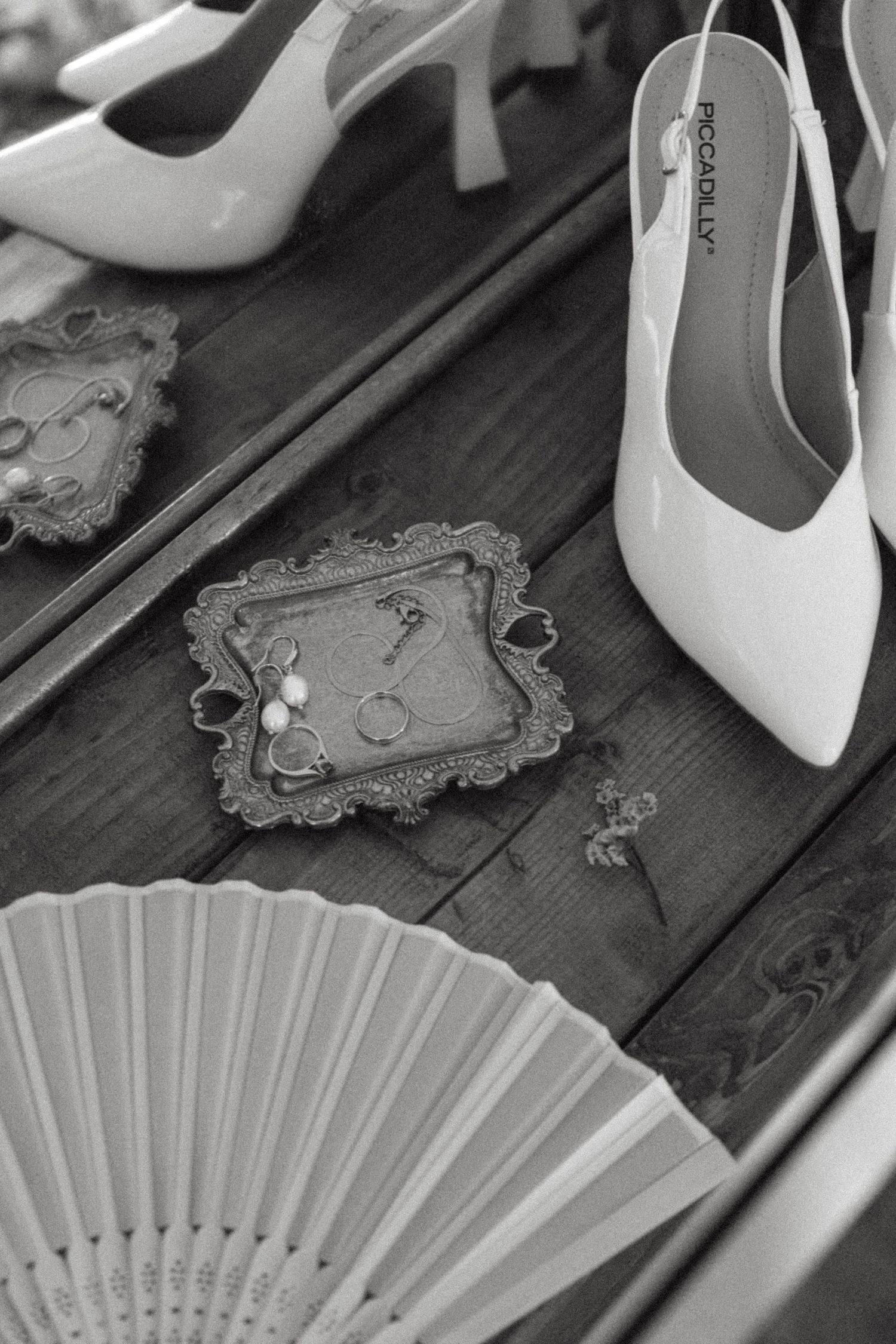 Wedding accessories including white heels, decorative fan, and vintage frame on wooden surface.