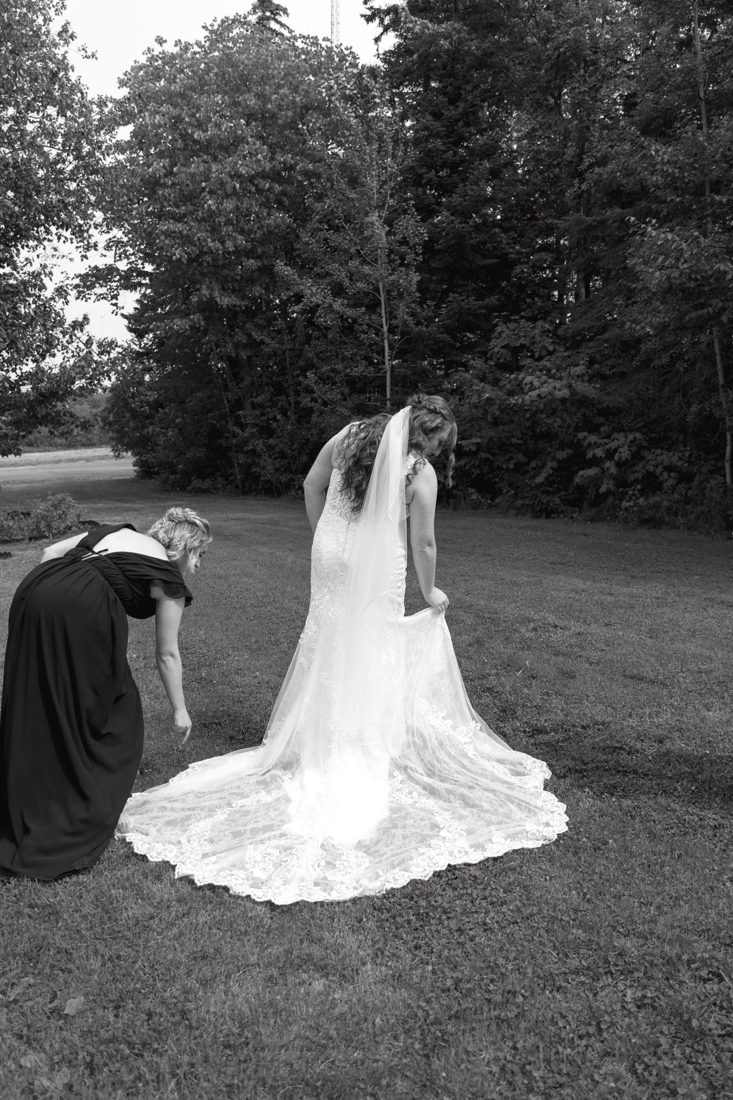 A wedding dress train being arranged on grass with lace details in black and white photography.