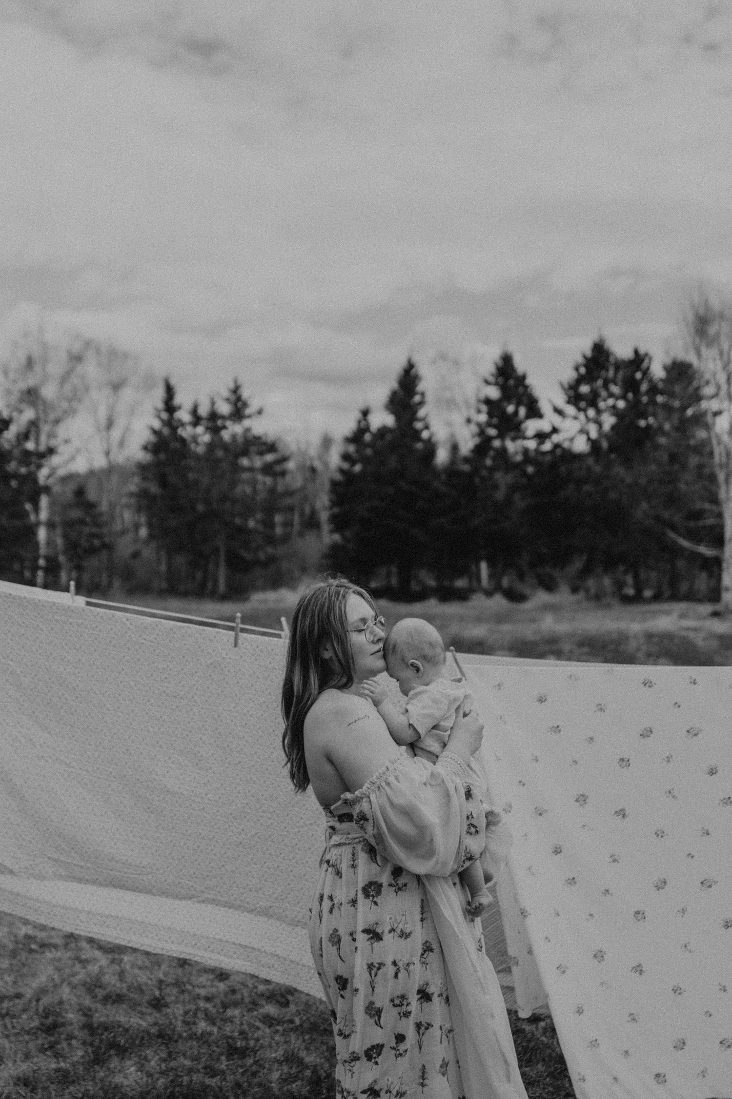 A tender moment captured in black and white as a parent holds a baby next to a patterned sheet hanging outdoors.