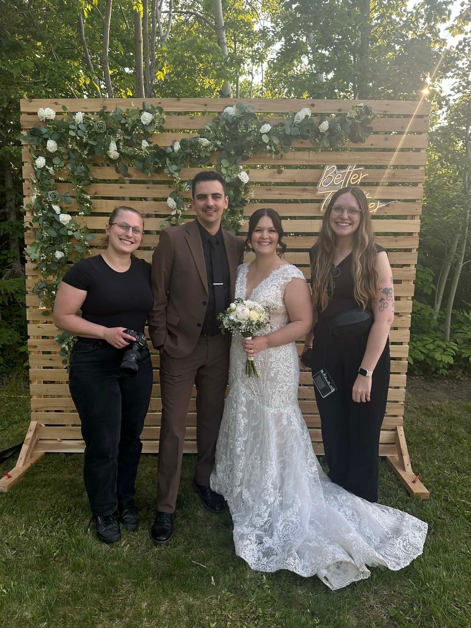A group of people pose together outdoors against a rustic wooden pallet wall backdrop at a garden event.
