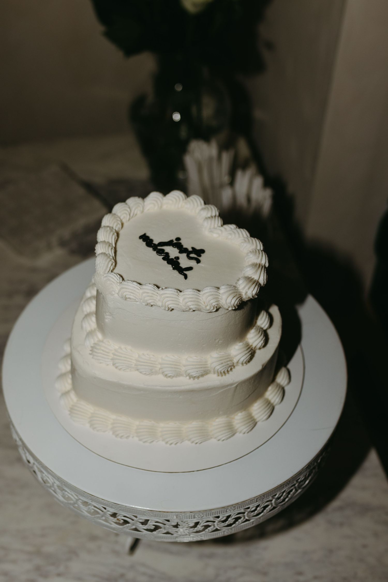 A three-tiered white wedding cake with a silhouette topper sits on an ornate cake stand.