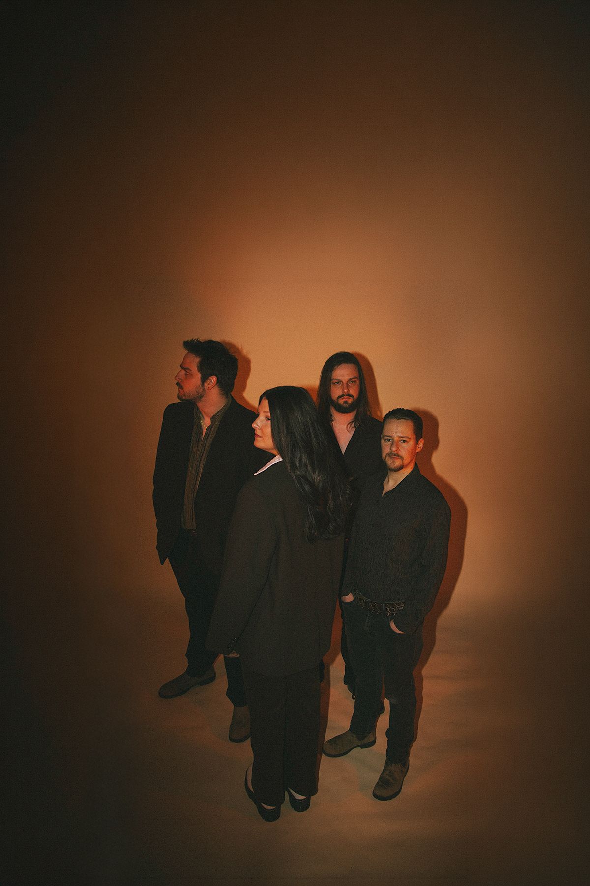 A group stands in silhouette against a warm brown background in an artistic portrait series.