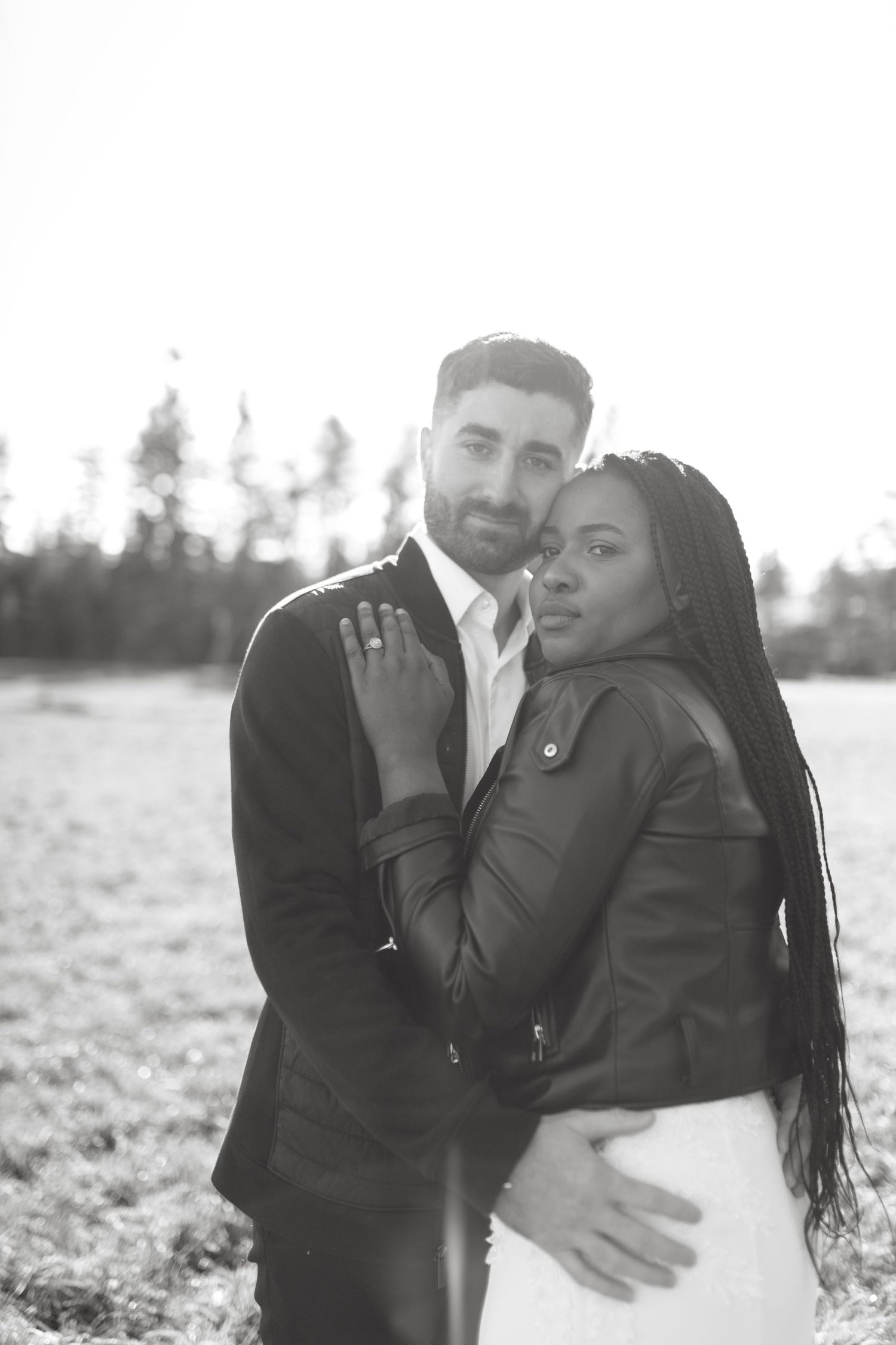 A romantic black and white portrait of a couple embracing outdoors with trees in the background.