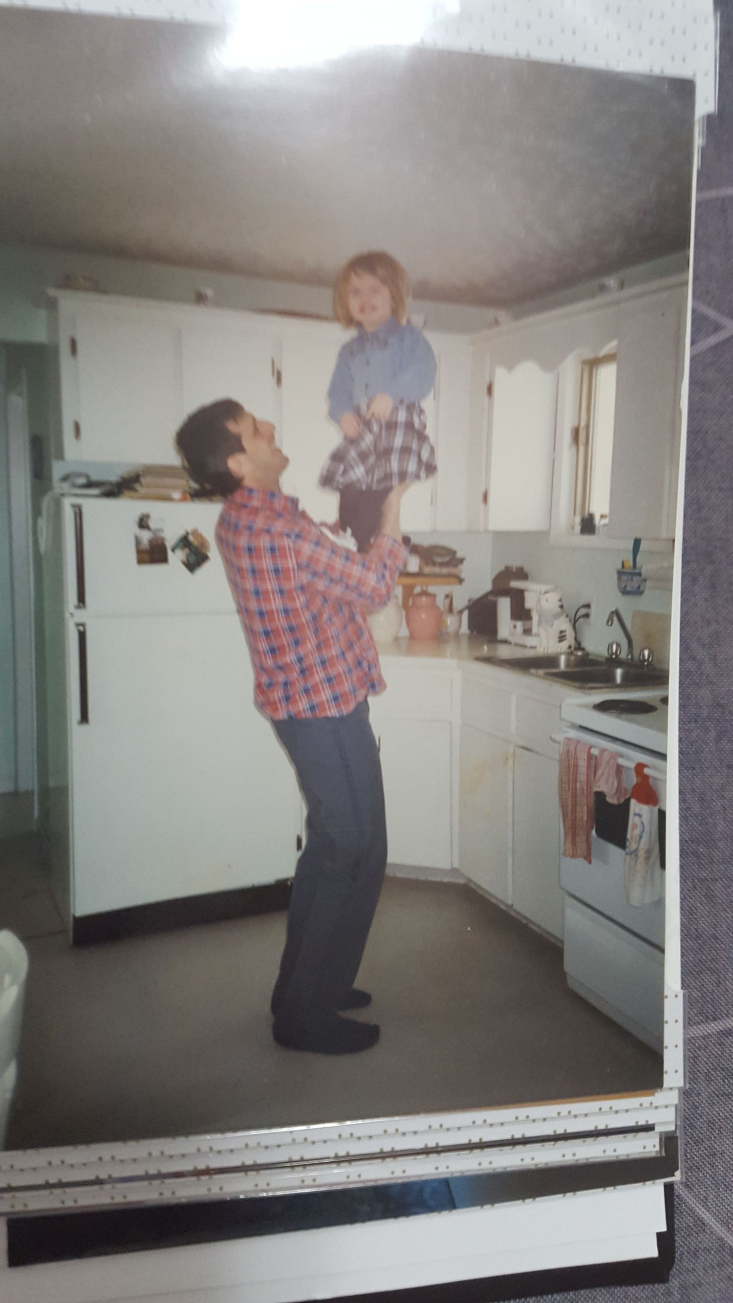 A heartwarming moment in a vintage kitchen as a parent lifts a small child high in the air while both wear plaid shirts.