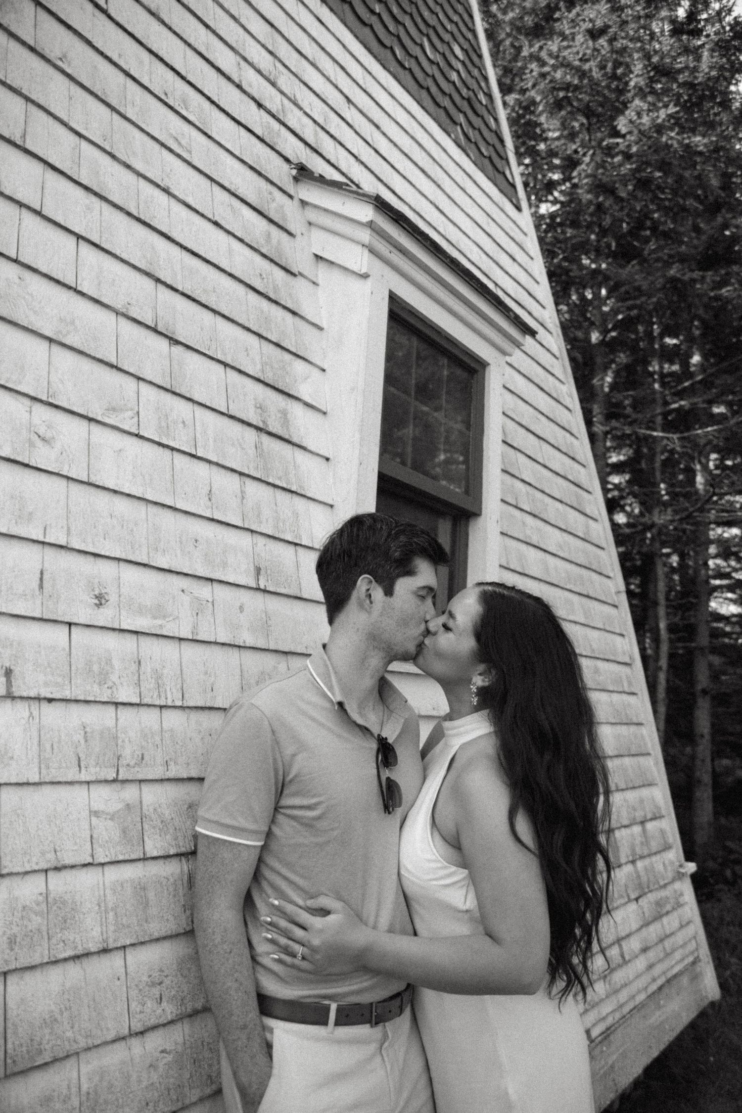 Romantic couple sharing tender moment against white building exterior.