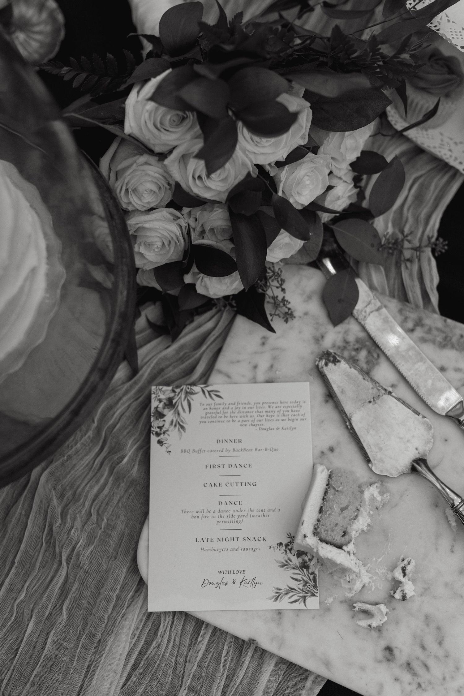 Wedding invitation cards displayed with delicate white roses and floral arrangements in black and white.