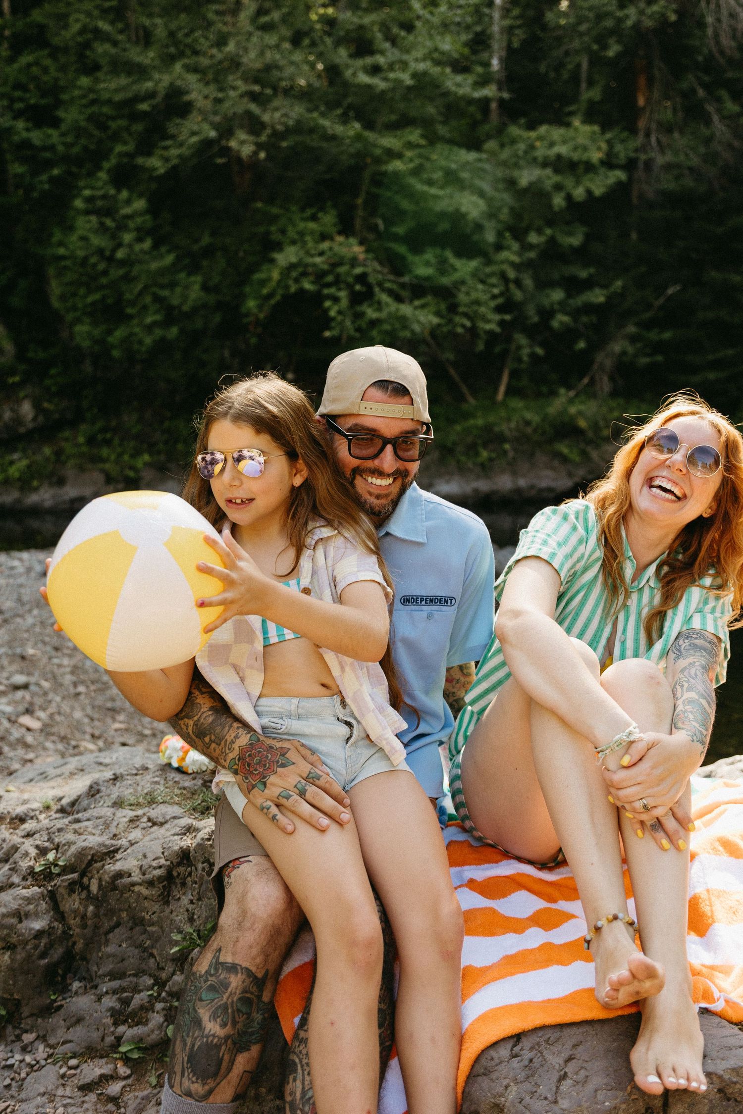 A group of friends relaxes on rocks by the water with a beach ball on a sunny summer day.