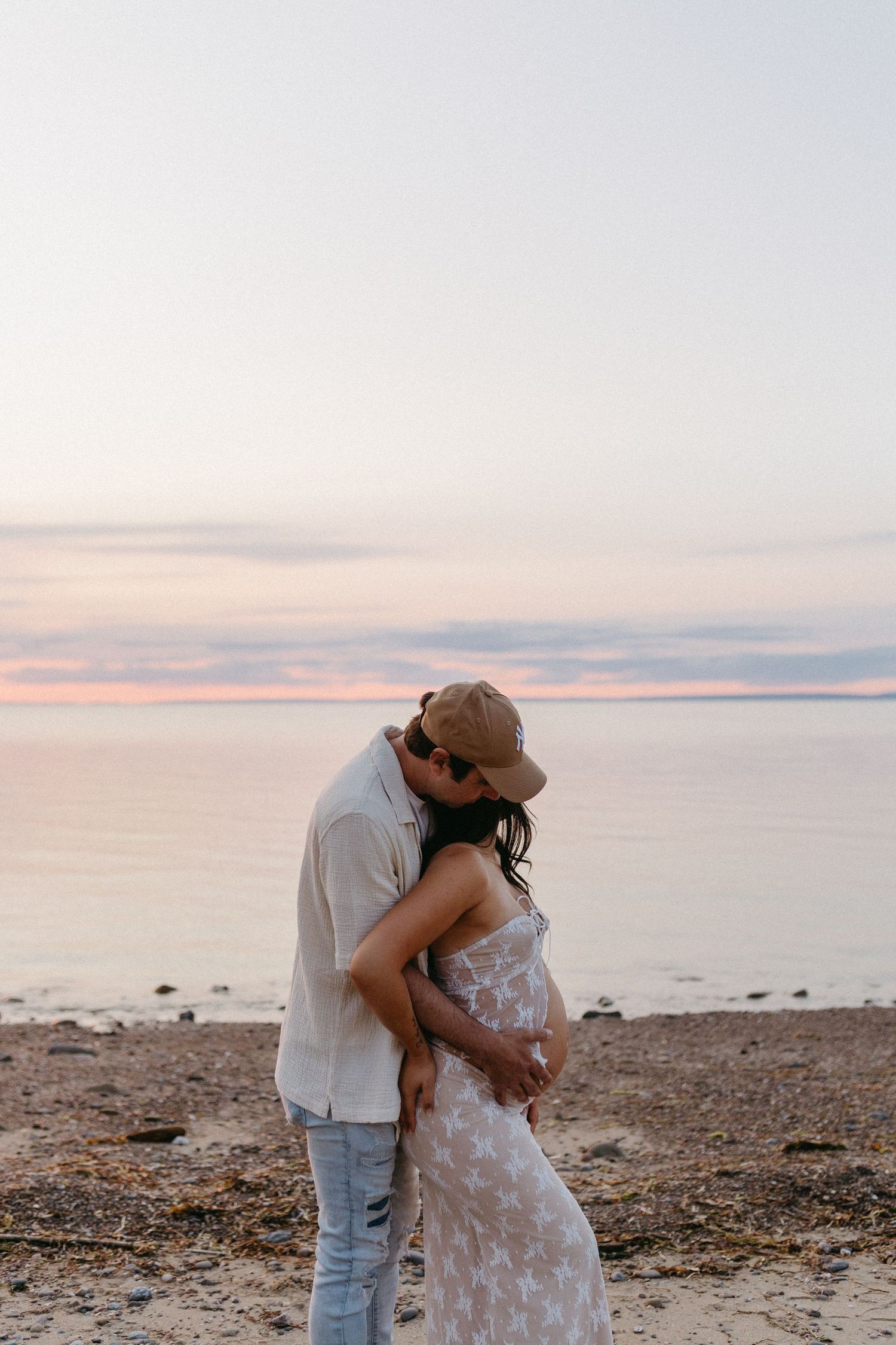 A romantic beach sunset scene with a couple in casual attire sharing an intimate moment by the water.