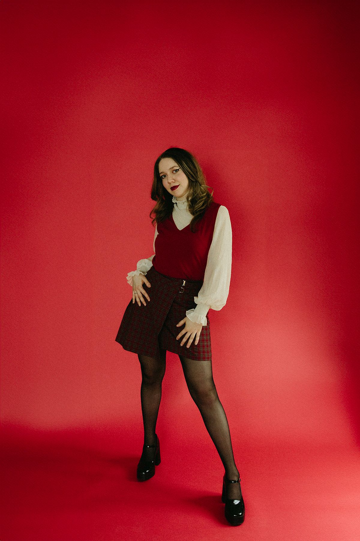 Figure in black outfit poses dramatically against vibrant red background in artistic photo series.