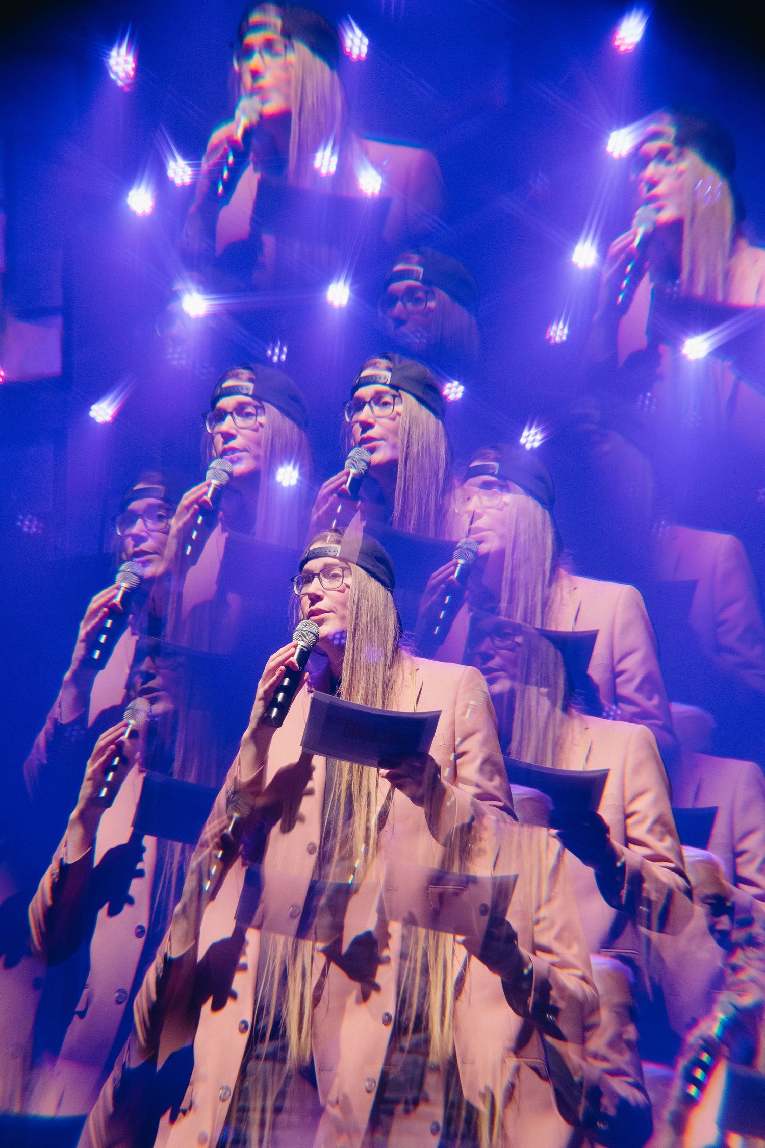 A choir performance in white robes illuminated by purple stage lighting during an evening concert.