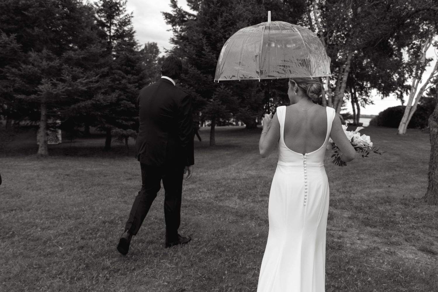 A couple walks through a park holding hands during a wedding photo session in black and white.