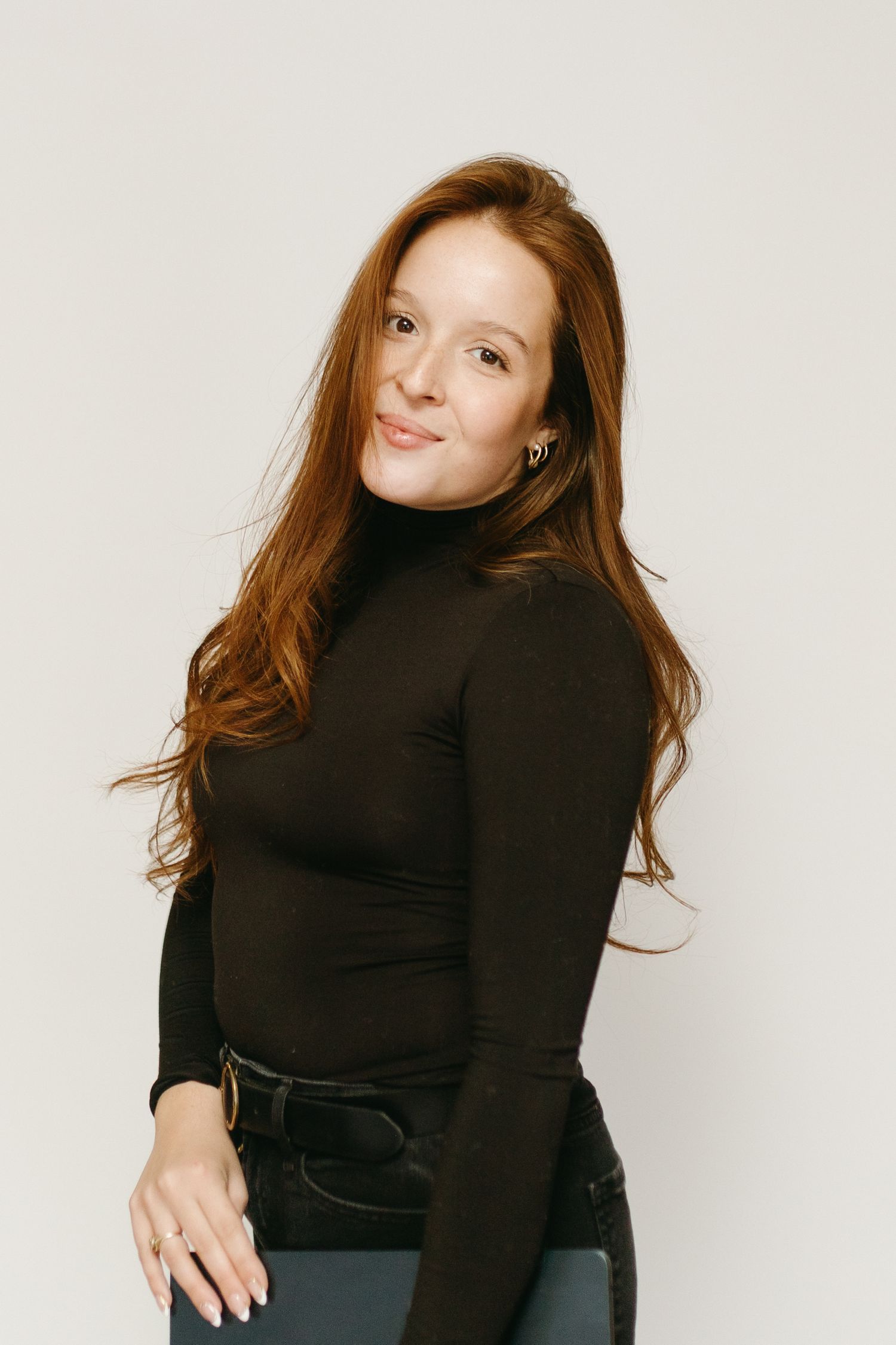 A person in a black turtleneck sweater poses against a light background with long flowing hair.
