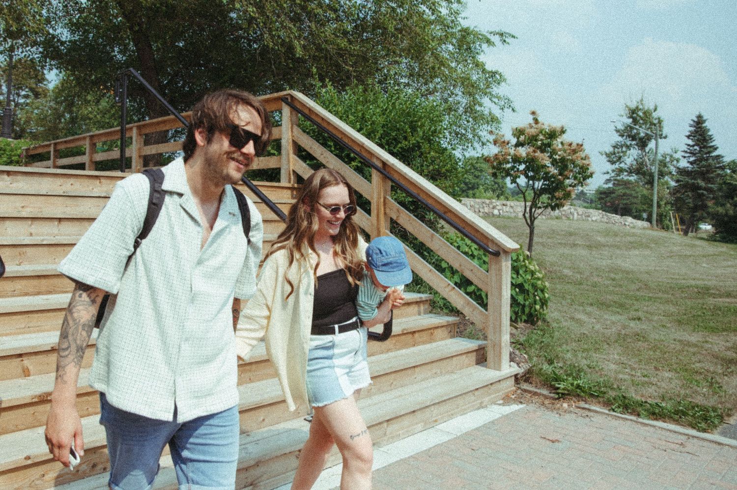 People walking down outdoor wooden stairs on a grassy hillside during a sunny summer day.