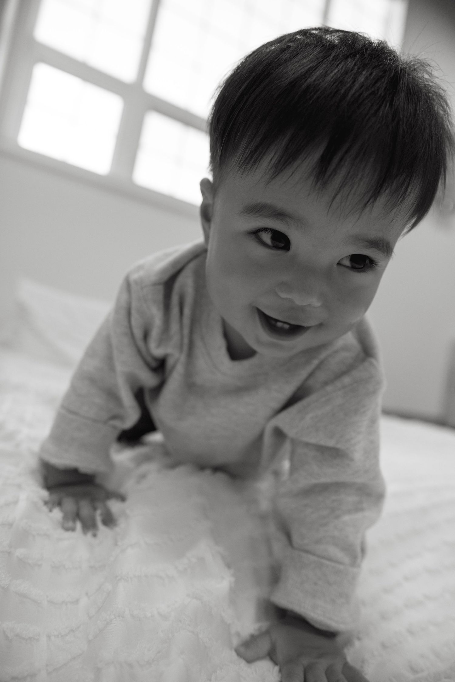 A sequence of five black and white photos showing a baby in white clothing making playful expressions on a light surface.
