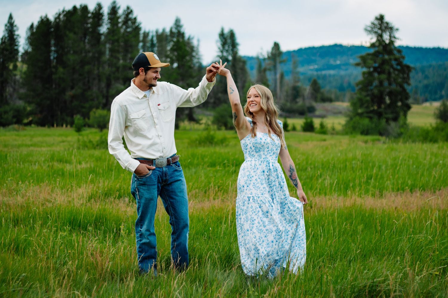 Couple dancing joyfully in a green meadow, man in white shirt spinning woman in a flowing blue floral dress.