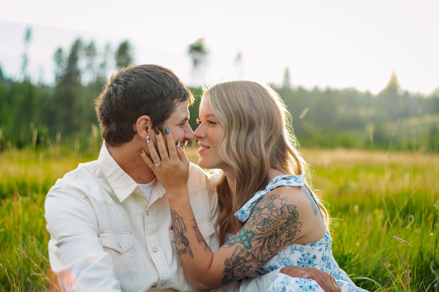 Tattooed couple sharing a romantic moment nose-to-nose in a sunny green field.