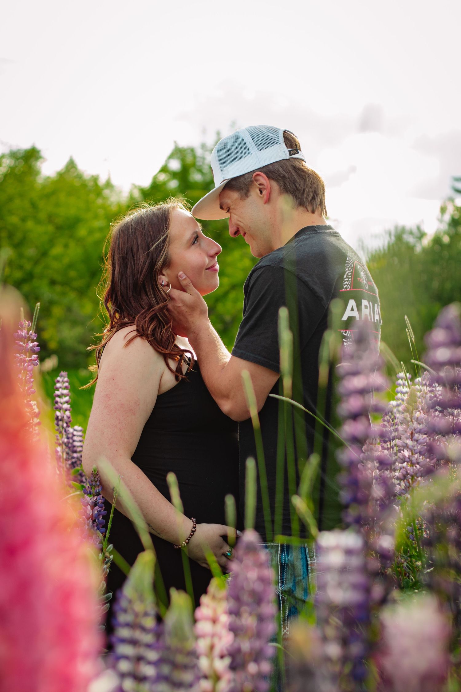 Expecting couple sharing a tender moment surrounded by colorful lupine flowers outdoors.