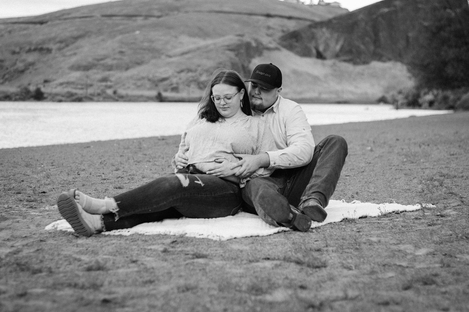 Black and white photo of couple sitting on beach blanket looking at ultrasound together.