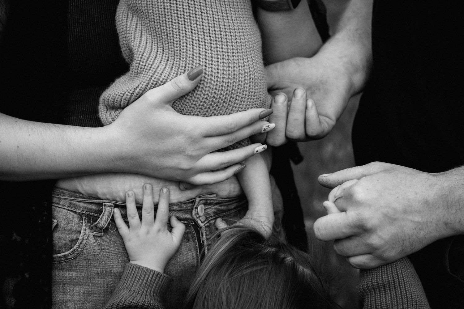 Black and white close-up of family hands touching a pregnant belly, symbolizing love and new beginnings.
