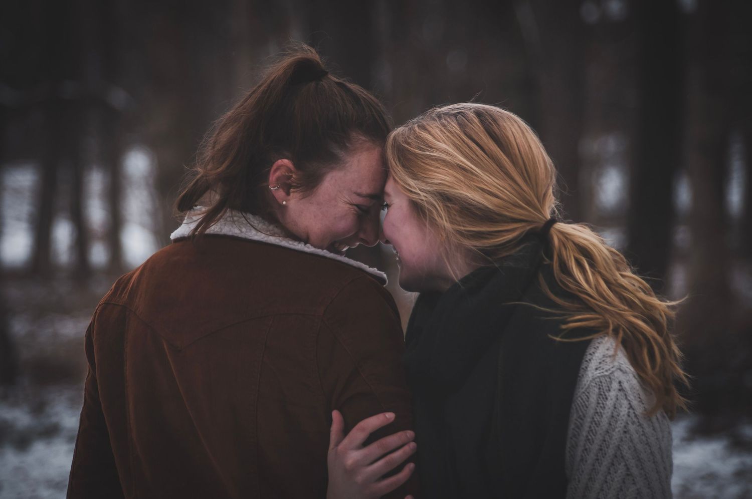 Queer couple staring lovingly into each others eyes in the snowy winter woods