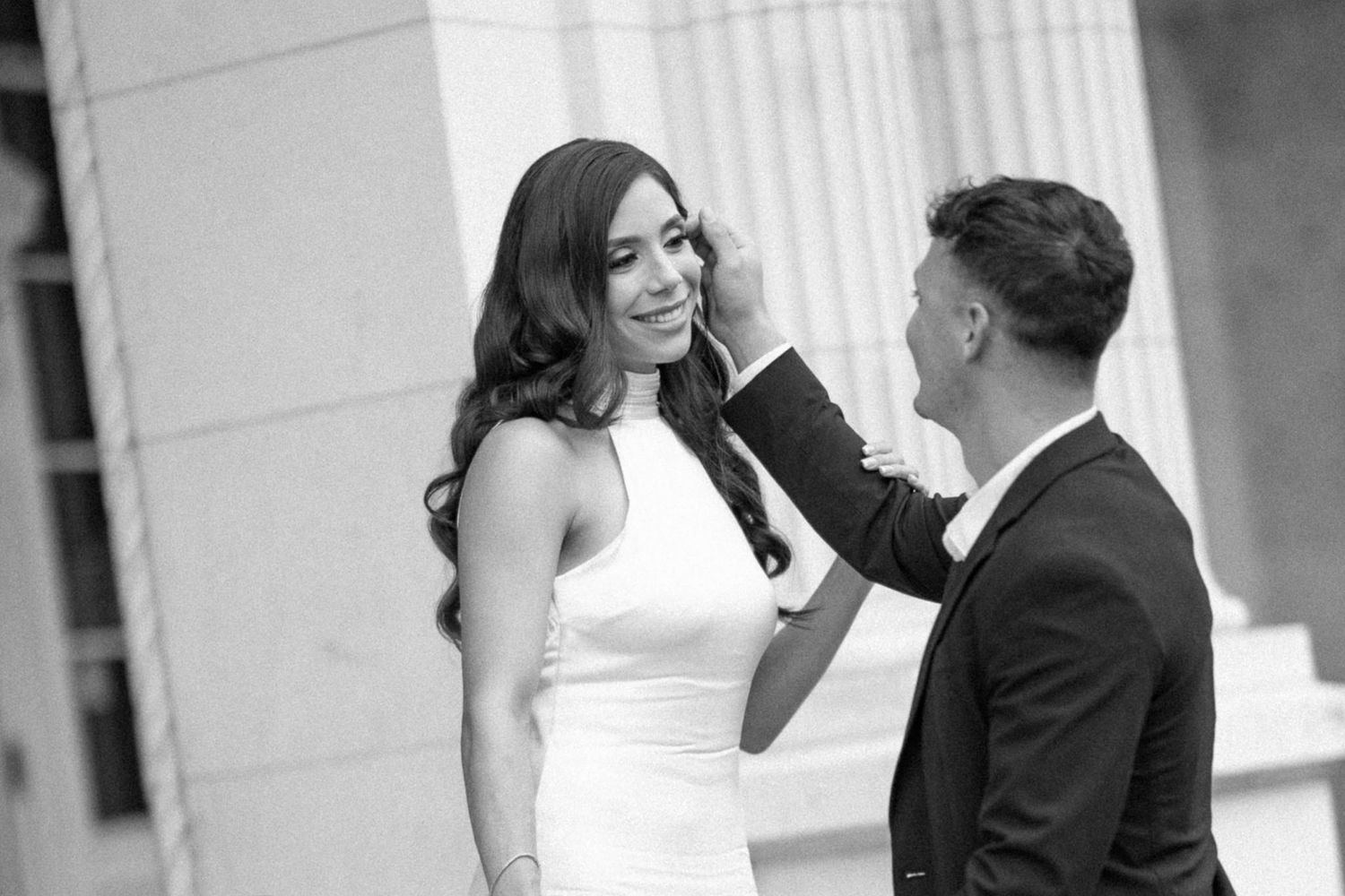 A romantic black and white wedding moment between a couple in formal attire against a classic architectural backdrop.