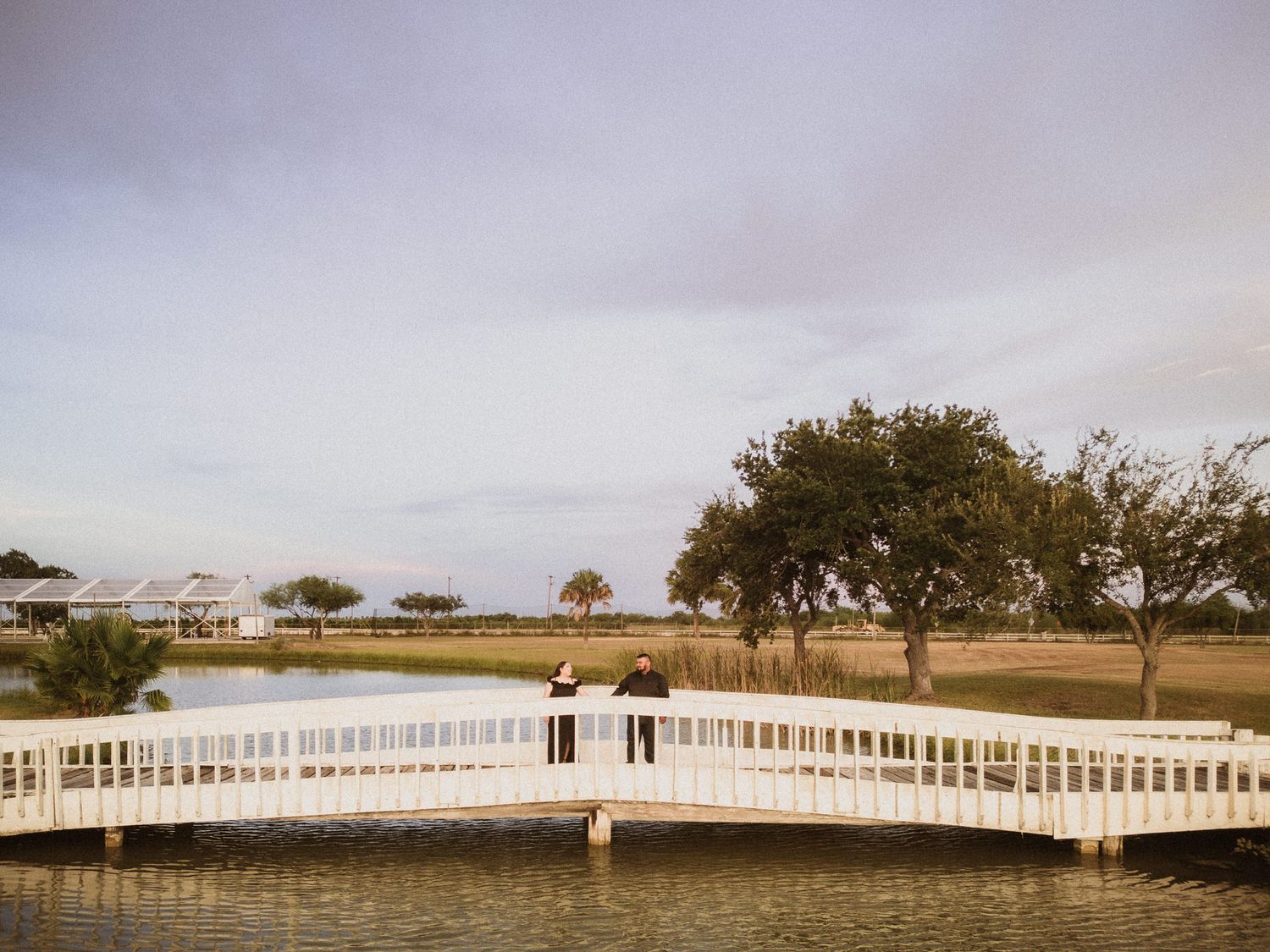 Wedding couple standing on white bridge over water during sunset.