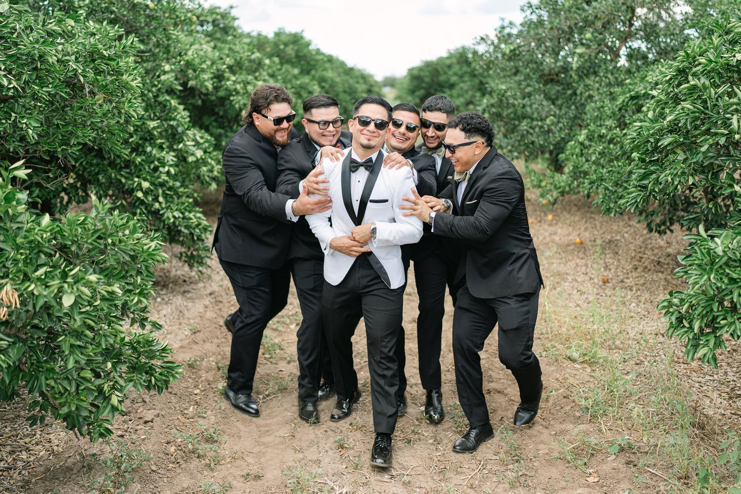 Groomsmen in black suits pose playfully in an outdoor garden setting.