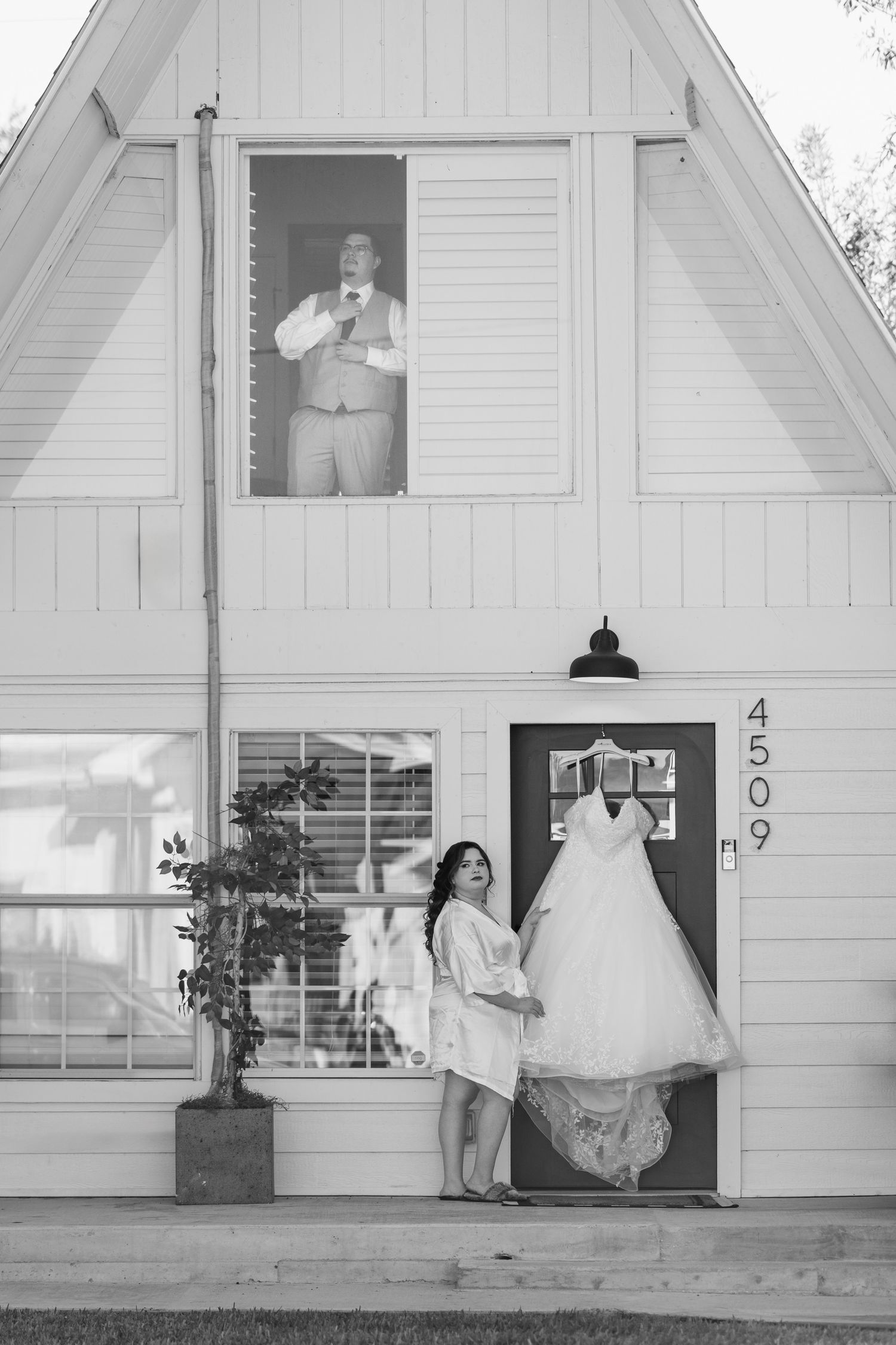 Black and white photo of a wedding dress displayed outside a white A-frame building.