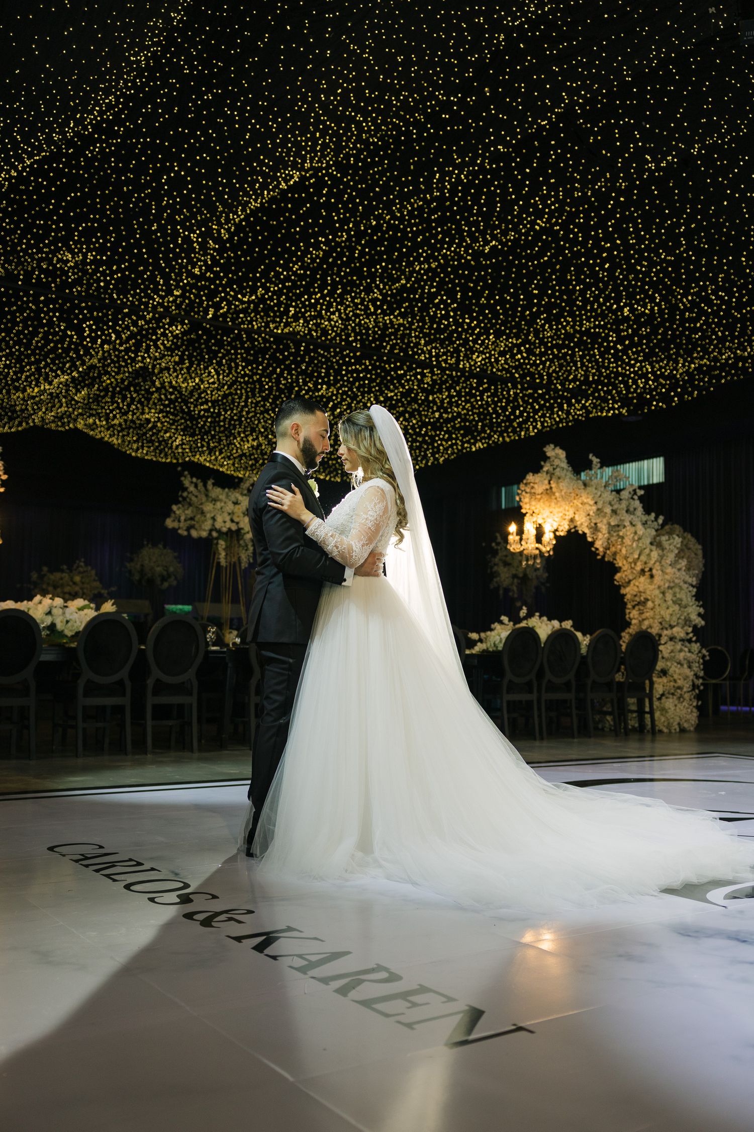 Bride and groom share first dance under starlit ceiling at elegant wedding reception with white floral decor.
