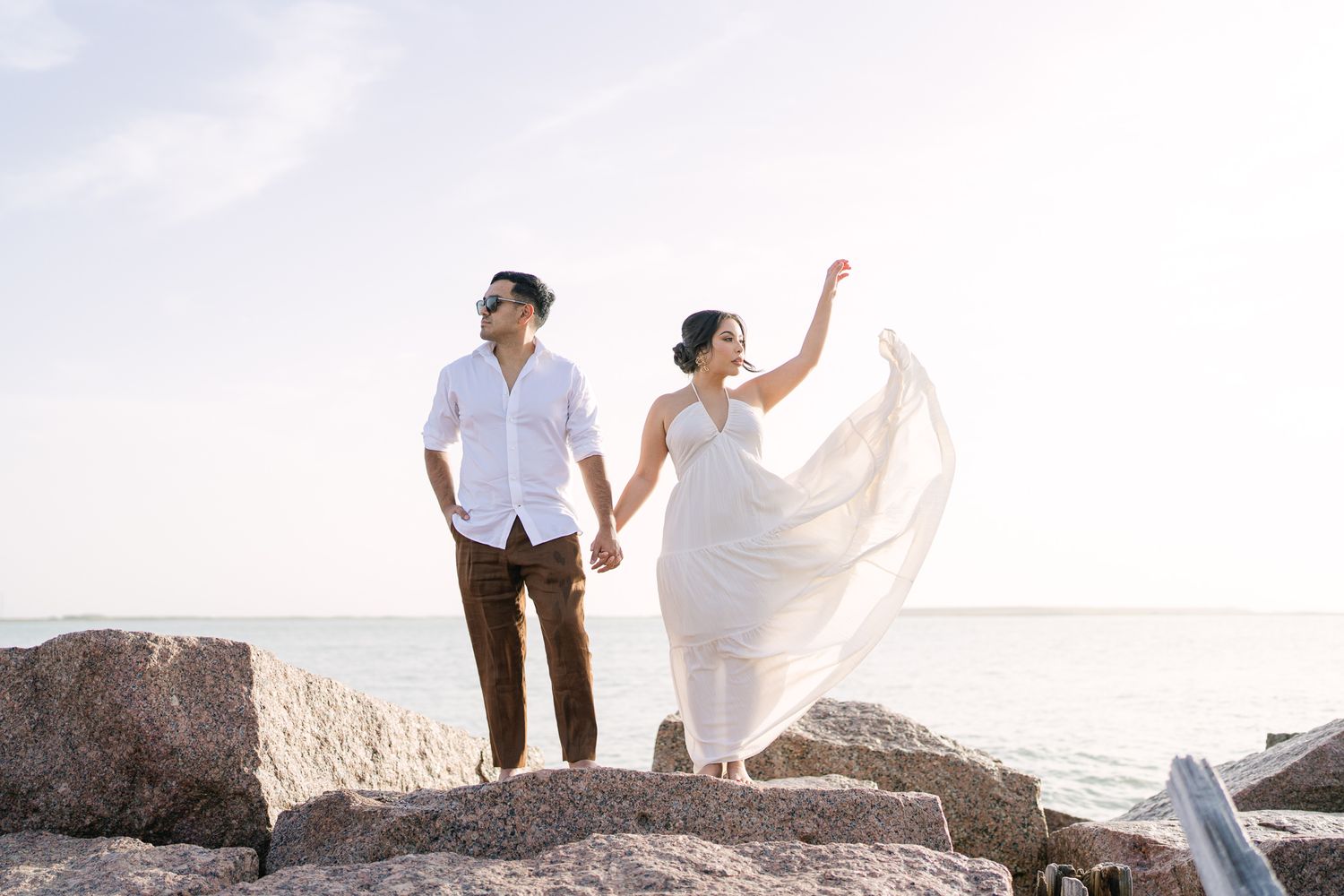 Couple stands atop rocky terrain during dramatic sunset photoshoot.