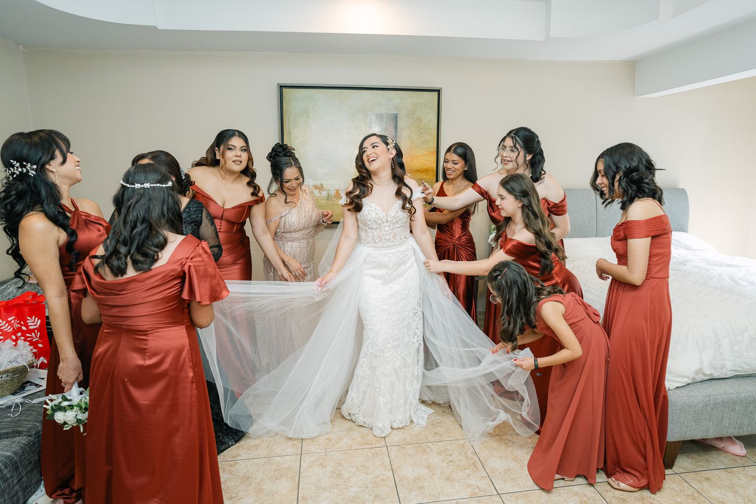 Wedding party in red dresses surrounds bride in white gown during pre-ceremony preparations.