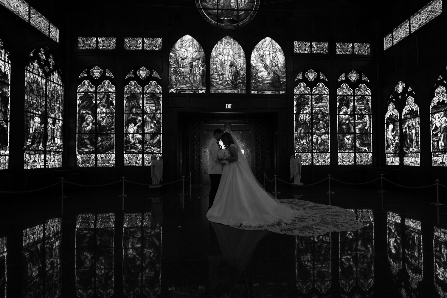A dramatic black and white wedding photo in a church with stained glass windows creating reflective patterns.