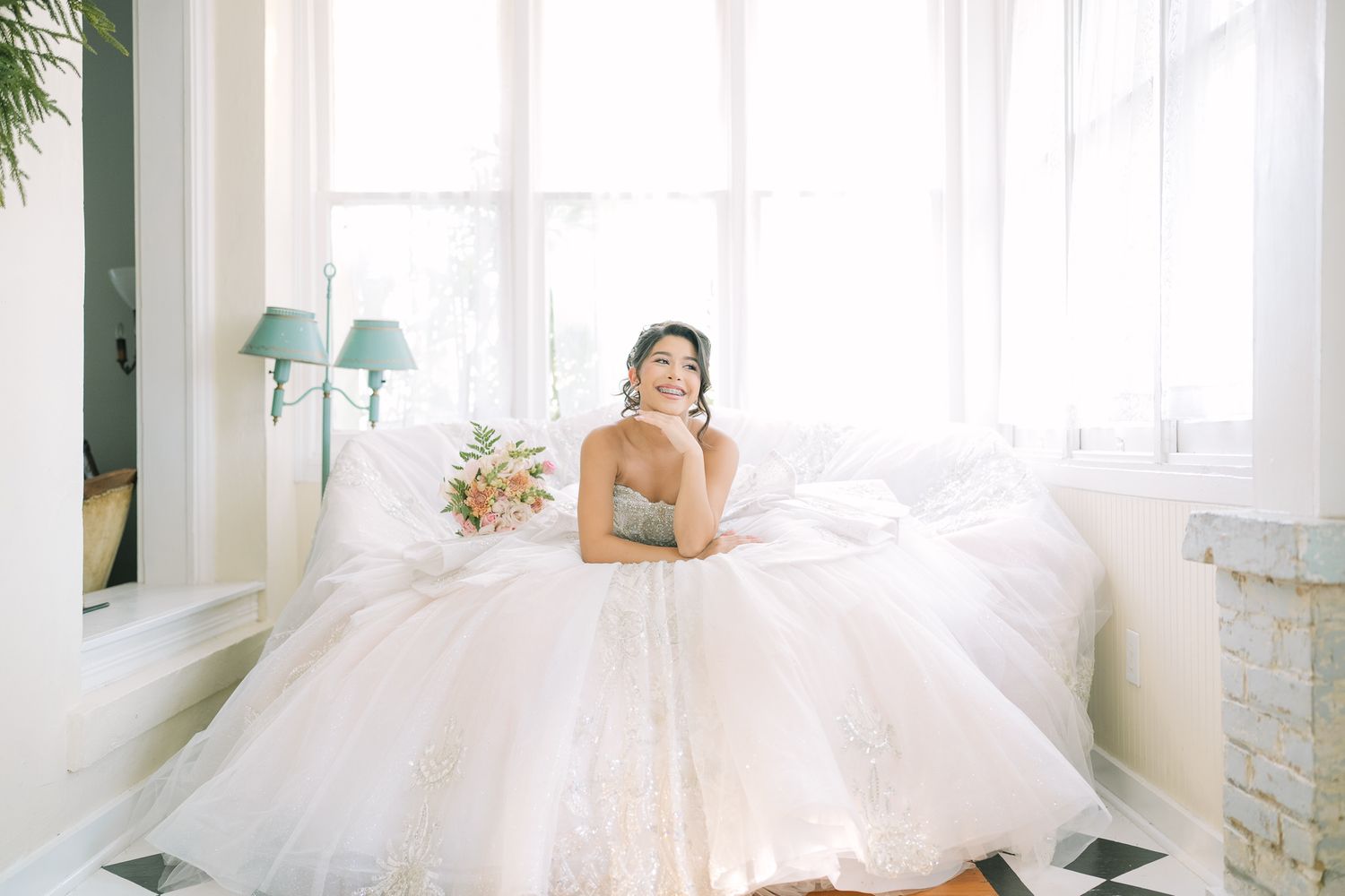 A dreamy bridal scene with flowing white tulle dress and soft natural lighting in an elegant white room.