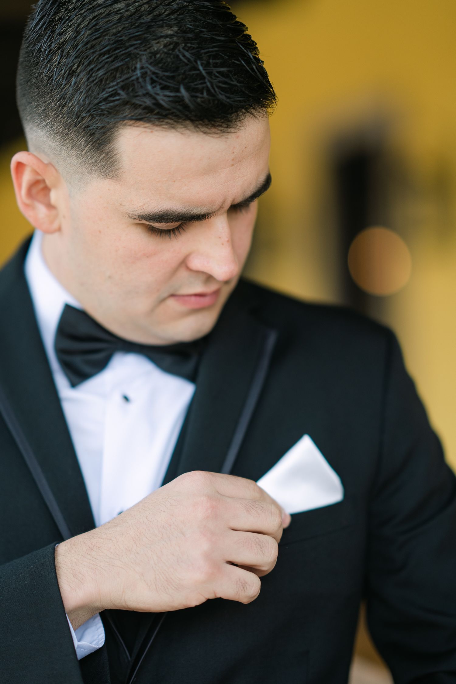 Groom in black tuxedo adjusts pocket square before ceremony.
