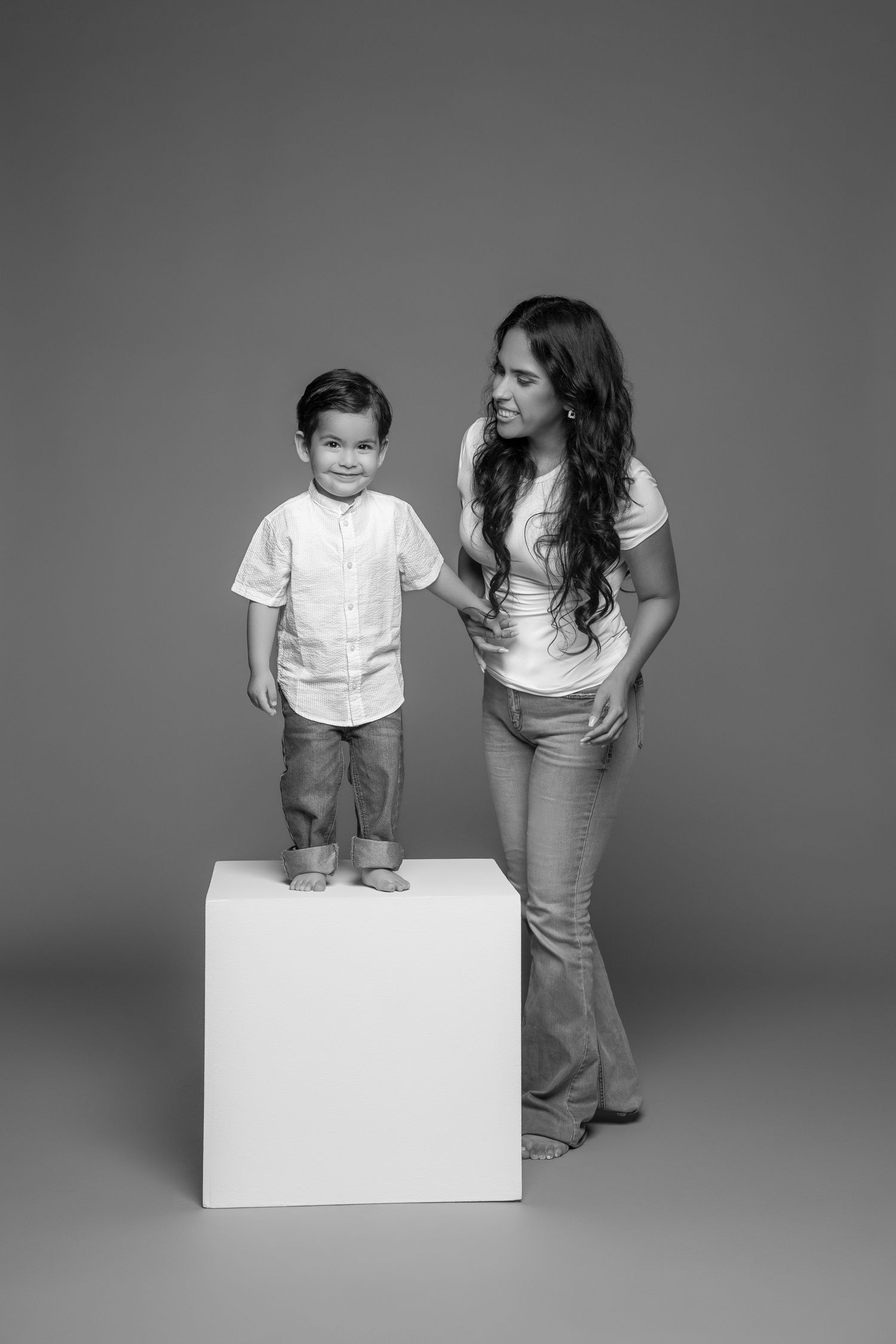 Studio portrait of parent and child standing by white cube against grey background.