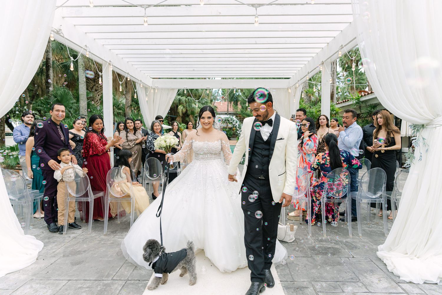 Newlyweds make joyful exit under white draped pavilion while guests celebrate.