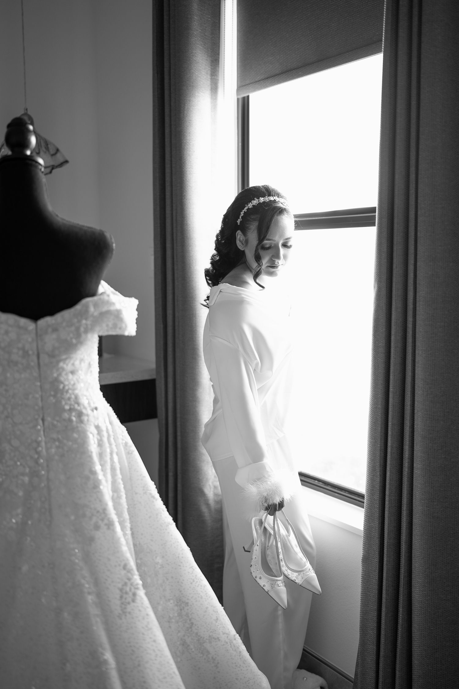 Wedding dress hanging by window with silhouette creating dramatic backlighting.