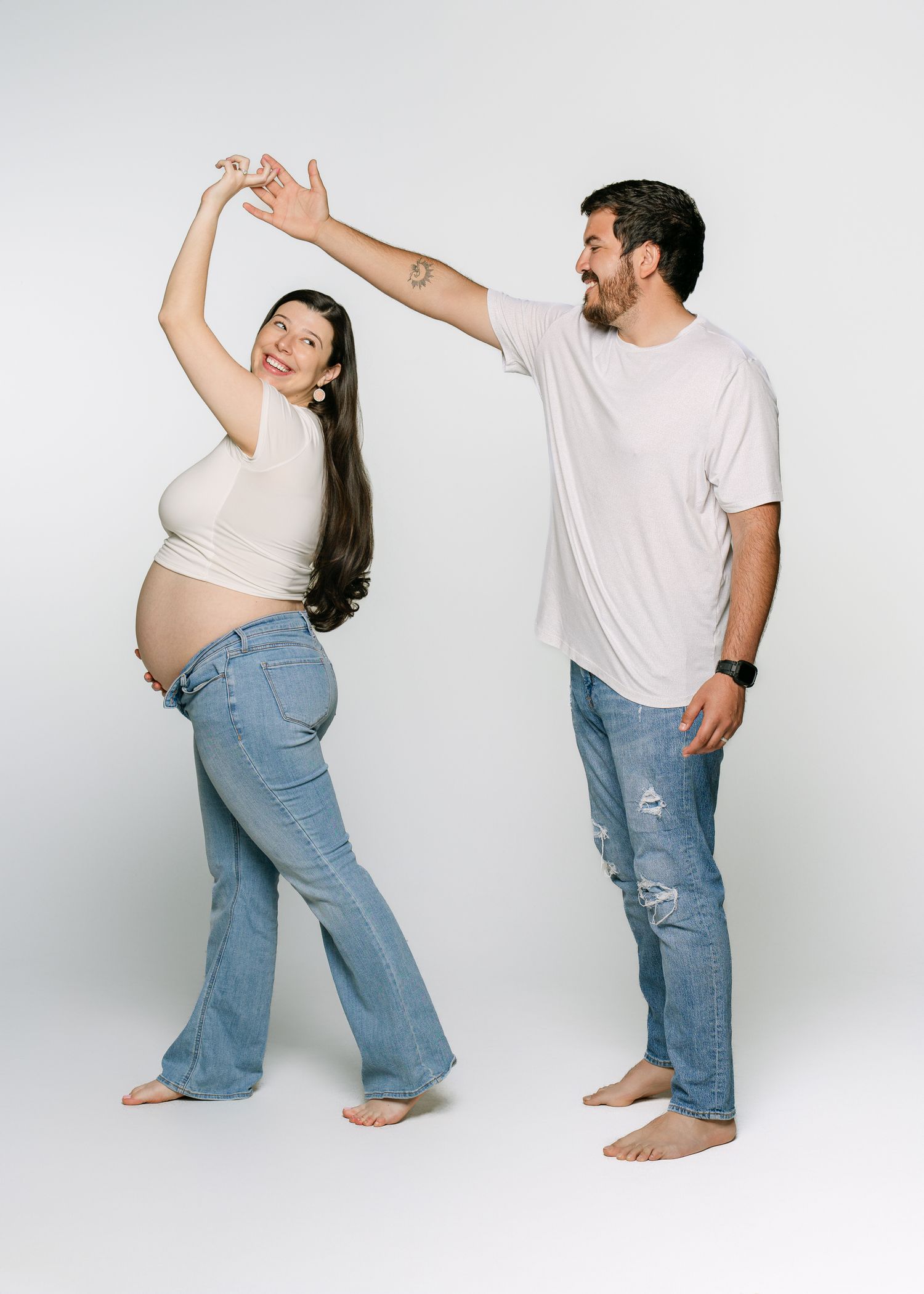 Playful couple dancing together during casual maternity photoshoot in studio.