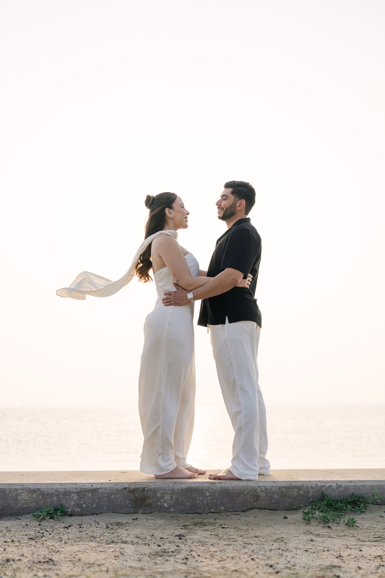 Couple in white clothing dances playfully on beach during sunset.