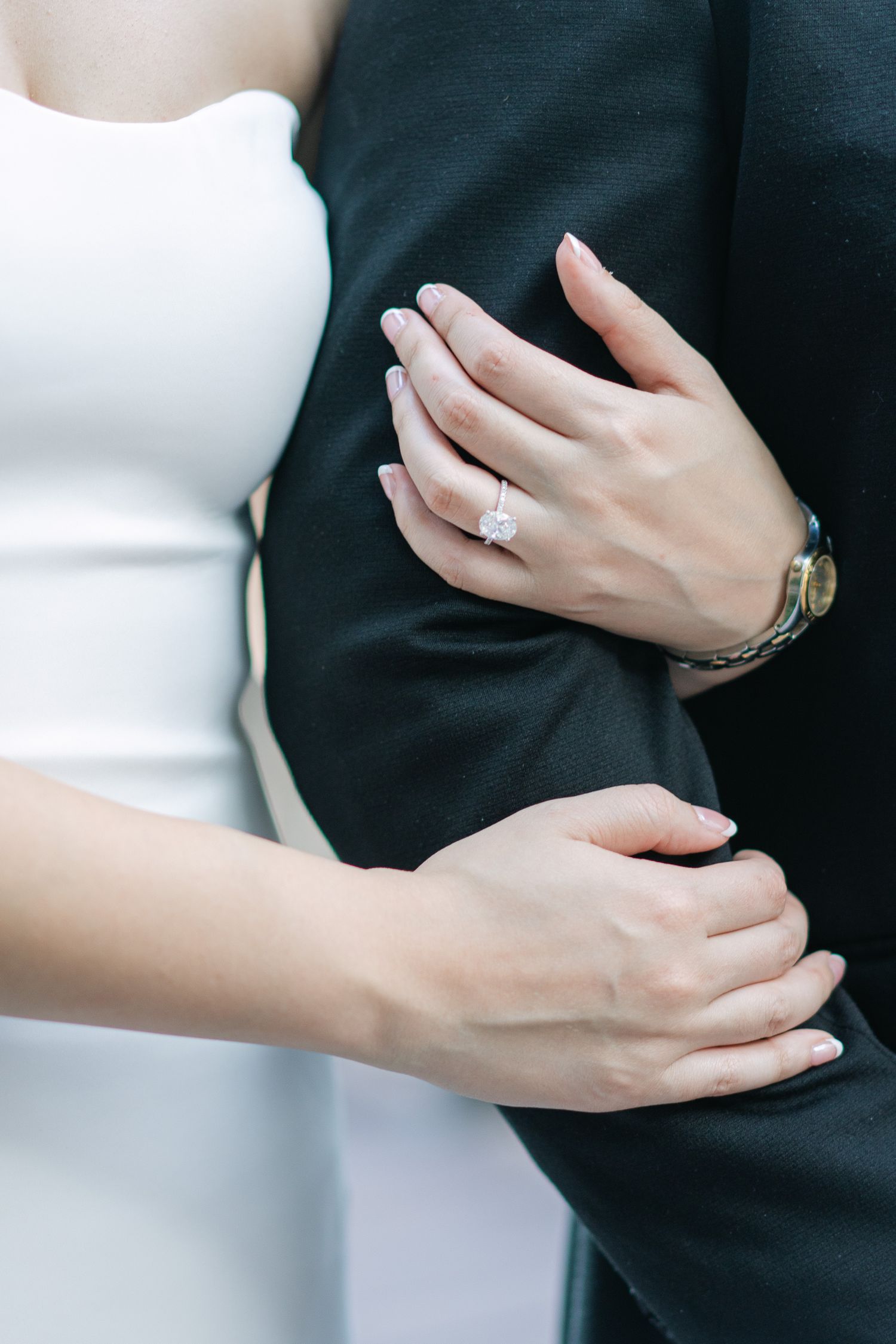 Close-up of hands wearing an engagement ring and watch against formal attire.