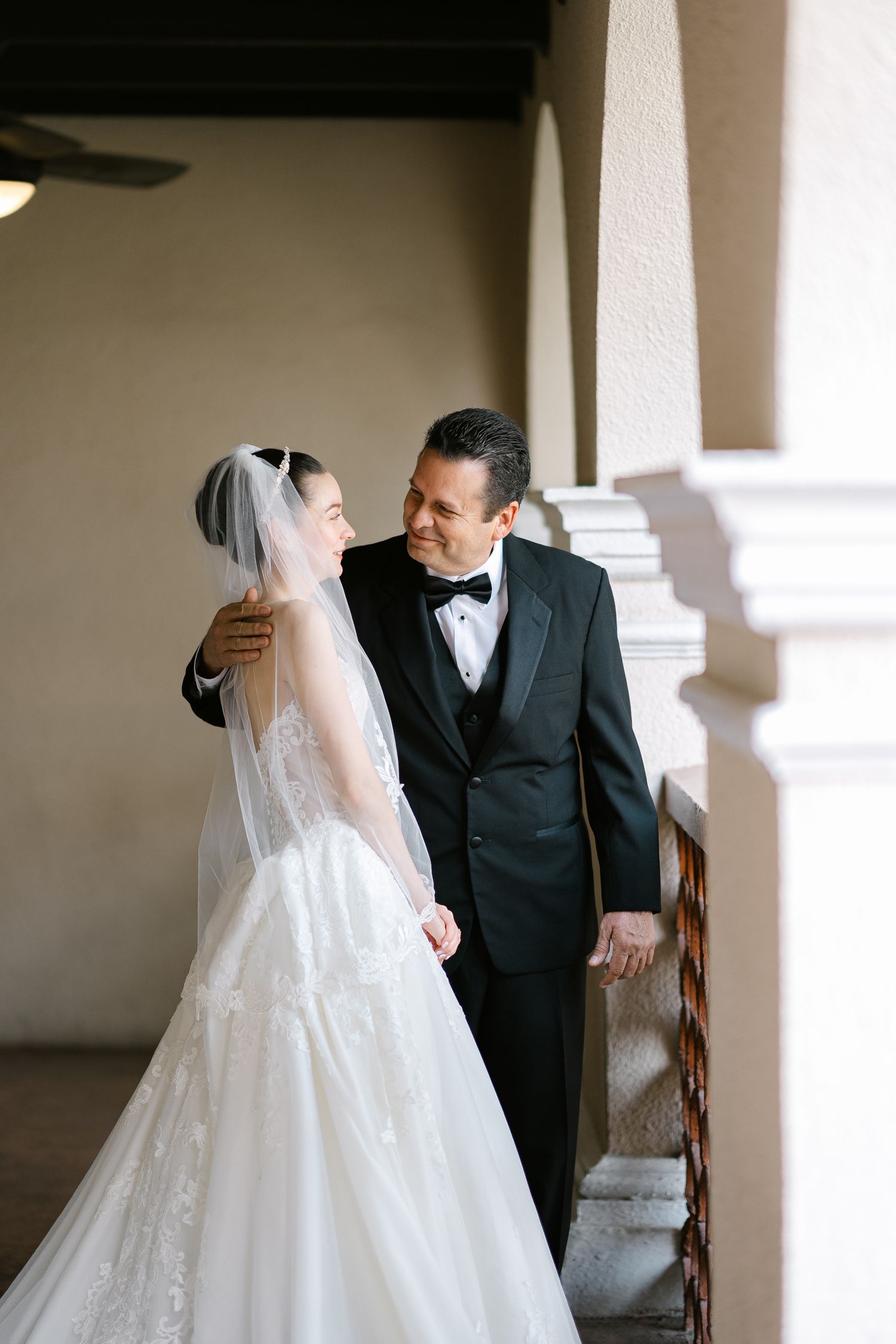 Couple sharing intimate moments in formal wedding attire near a columned interior.
