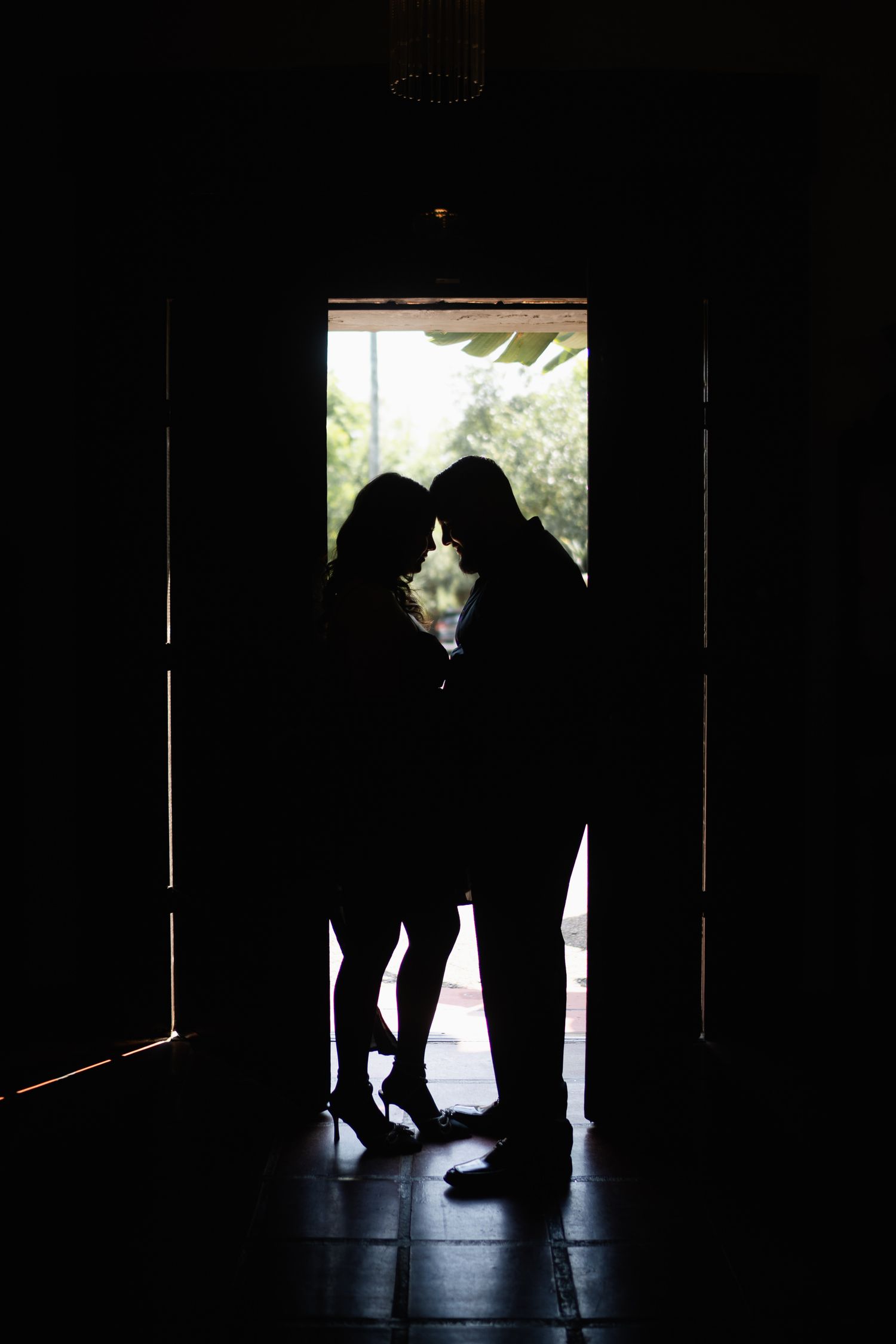 Romantic silhouette of couple standing in doorway backlit by natural light.