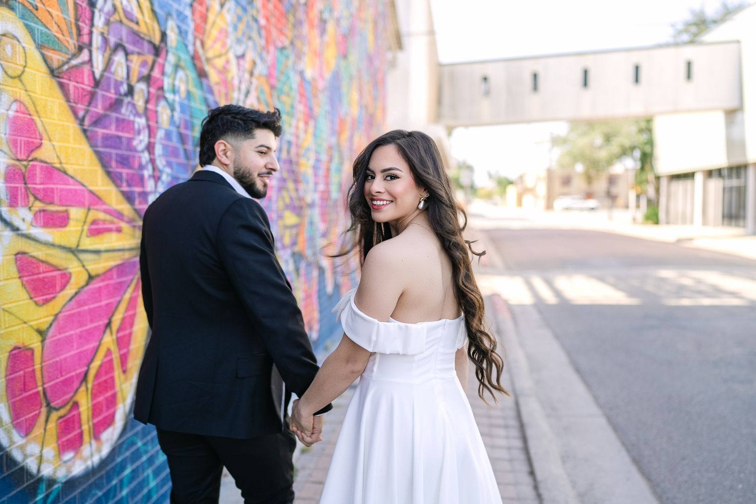 A couple in wedding attire poses in front of a vibrant street art mural.