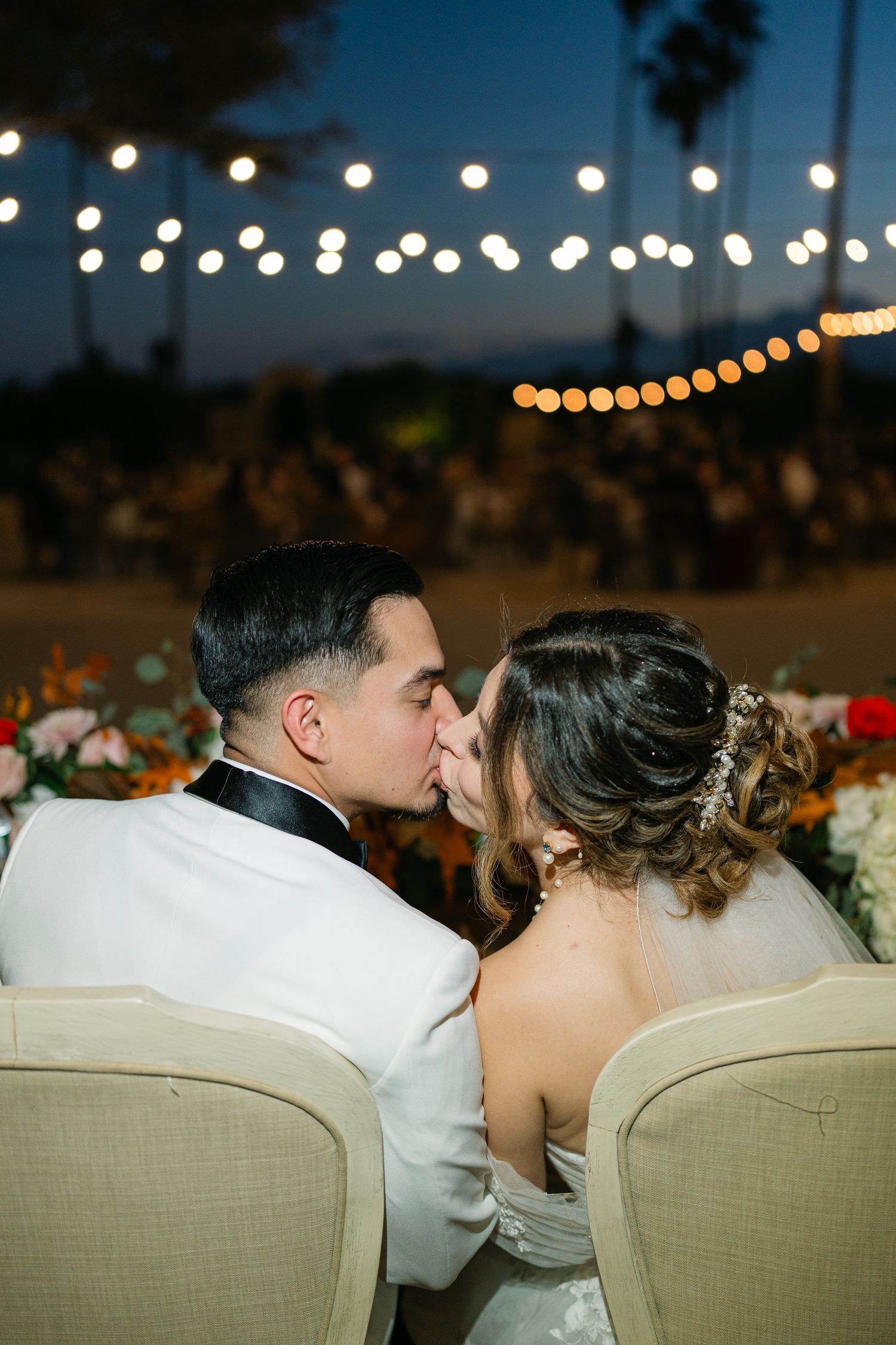 Romantic outdoor wedding scene with string lights overhead as couple shares intimate moment.
