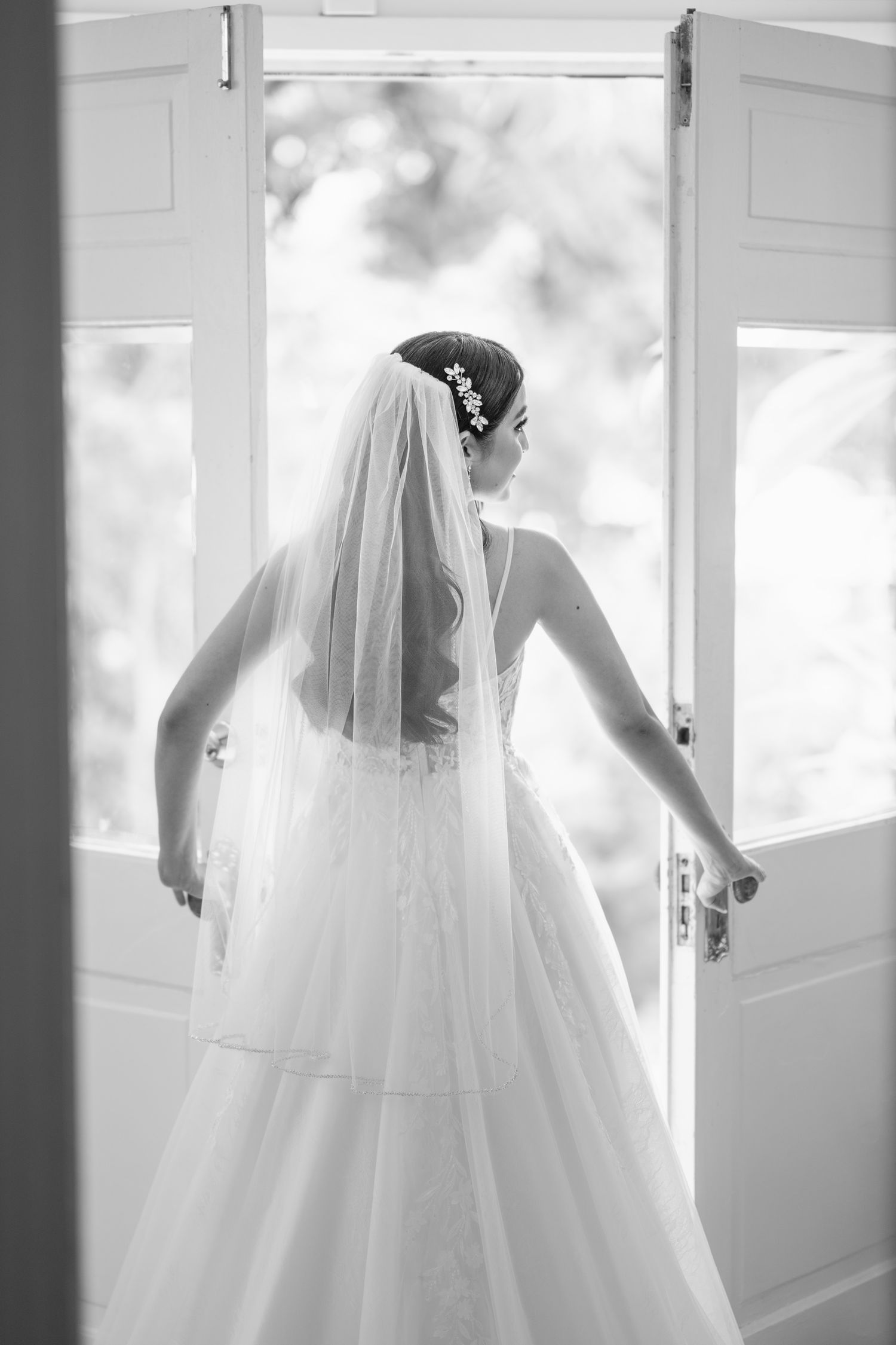 Ethereal bridal silhouette in flowing white gown against window light.
