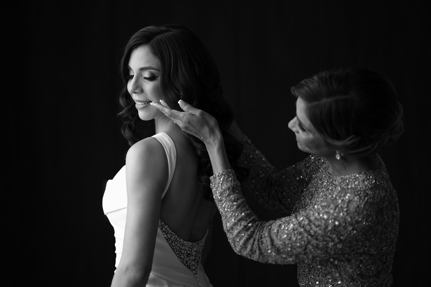 Black and white image of bride getting ready with help adjusting veil.