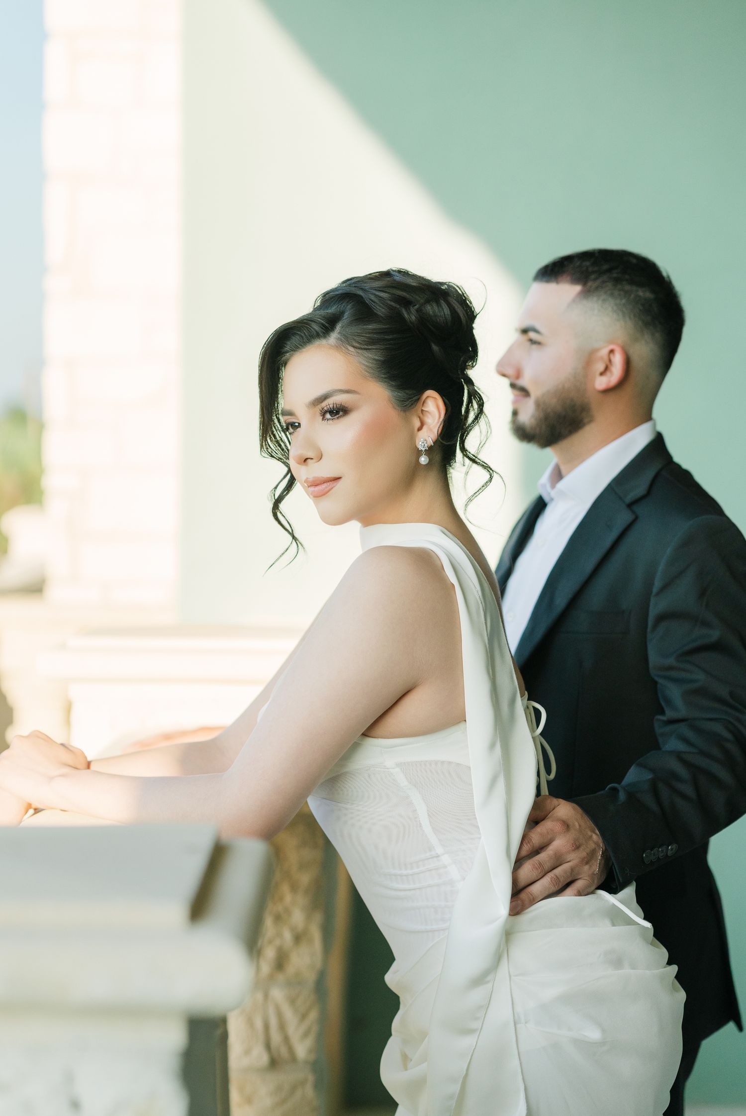 A bride and groom pose together against a mint green wall during their elegant wedding photoshoot.