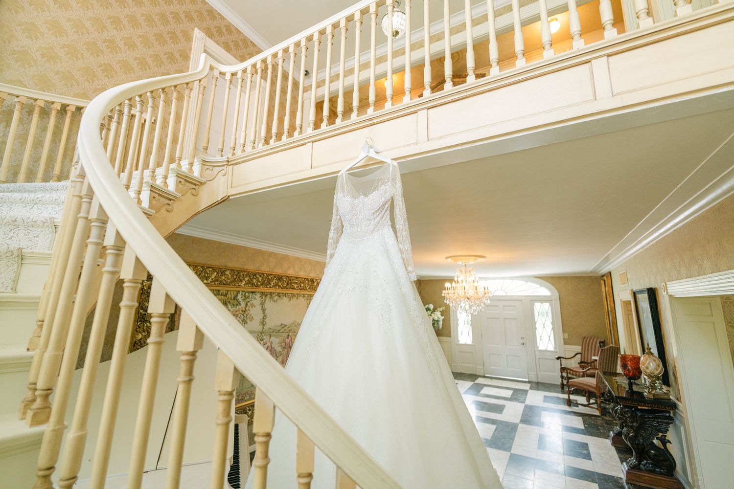White wedding dress hangs elegantly on curved staircase in bright interior setting.