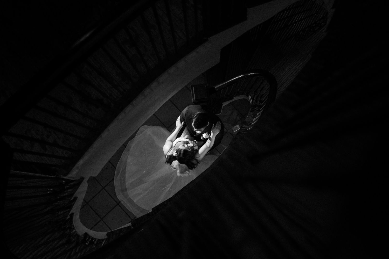 Artistic black and white overhead shot of a couple on spiral stairs.