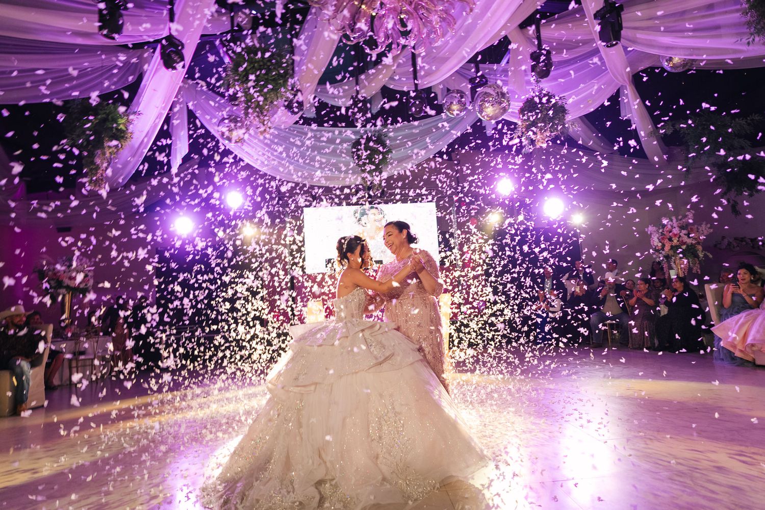 A couple dances under purple lights and falling confetti during a romantic wedding reception celebration.